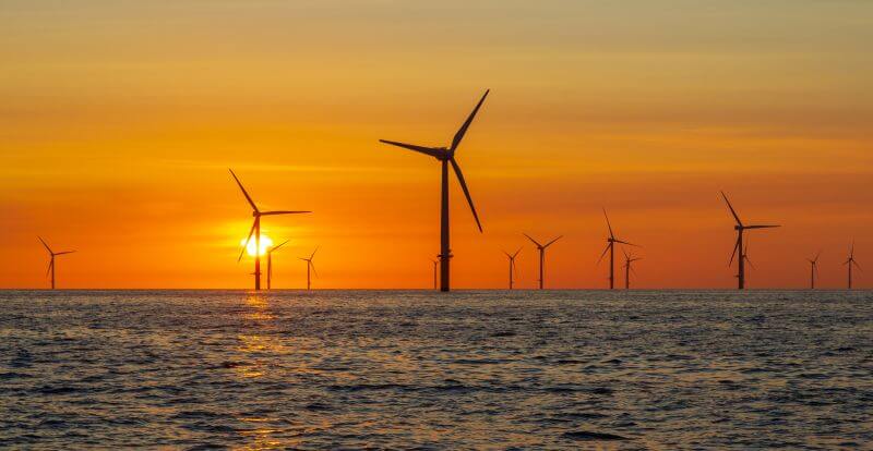 Wind turbines out at sea, with sunset in background